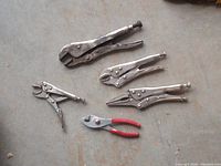 Five pliers on a concrete floor, four vise grips, one slip joint with red handles.