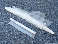 Two rolled up pieces of translucent white vapor barrier plastic sheeting laid on gravel ground, one larger and partly unrolled, the other smaller.