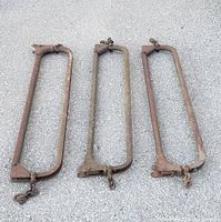 Three vintage metal cow stanchion frames arranged side by side showing their size and condition with visible rust and chained ends.