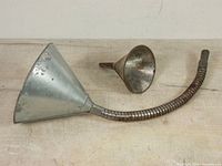 Top view of two vintage fuel funnels, showing large funnel with flexible coiled spout and smaller funnel beside it.