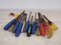 Overview of all 11 woodworking chisels with different handle colors and sizes laid out horizontally showing condition and types.
