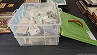 Two plastic bins with numerous smaller clear plastic bags, containing various vintage jewelry pieces, mostly earrings, necklaces, and pendants