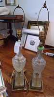Pair of two 32 inch crystal lamps shown together on a wooden floor with various frames in the background, no shades, metal harp for shade support visible.