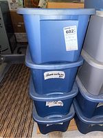 Four stacked blue plastic storage bins labeled for curtains and shower curtains