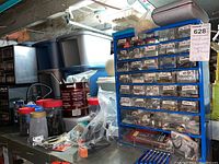 Wide view of basement workbench with three hardware drawer units, jars, bags of small hardware, and tools including screwdrivers and clamps visible.