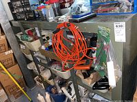 Shelf with orange extension cord coiled, hardware items, jars and other small tools and containers