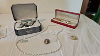Full view of all items including watches in Geneva box, Shaeffer pen and pencil set in red case, sterling silver necklace, and two brooches