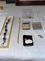 Full view of two bracelets/necklaces, multiple pairs of earrings on a white cloth background