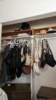 View of multiple purses and hats on a closet hanger and shelf, showing various styles and colors including black, beige, and brown purses along with straw hats.
