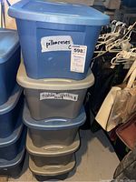 Plastic container labeled 'pillowcases' on top of container labeled 'tablecloths round' stacked in basement storage.