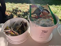 Photo of two white buckets side by side outside. One bucket contains individually packed marble sets. The other bucket contains a plastic bag with building blocks and the Mega Bloks instruction booklet on top.