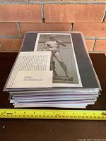 Stack of individually packaged and matted prints featuring classical artworks, measuring approximately 30 cm wide, shown against brick wall background.
