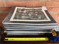 Stack of individually sealed matted prints showing top print with multiple nude figures in monochrome style, measuring about 15 inches wide.