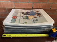 Stack of individually sealed and matted Norman Rockwell prints showing one with a scene of a man and boy in a store setting.