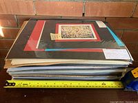 Stack of approx. 25 sealed art prints with measuring tape showing size about 12 inches wide