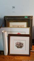 View showing six framed prints including one rolled print, frames stacked with visible design and wear.