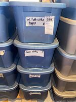 Stack of four labeled blue bins indicating table cloths and toppers inside