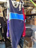 Photo of navy blue one-piece bathing suit with light blue and white horizontal stripe hanging on a white hanger among other clothing items in storage.