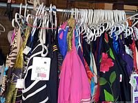 Photo showing multiple women's bathing suits hanging on a rack, various colors and patterns, all with tags indicating size 12.