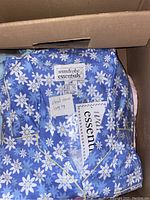 Box of folded women's pyjamas neatly packed showing blue floral pattern pyjama top with label Wardrobe Essentials and size large tag