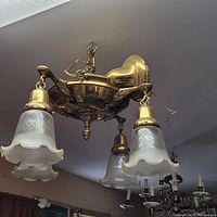 Photo of early 1900s brass pan chandelier mounted on ceiling with three pressed glass shades showing scalloped edges and etched floral design.