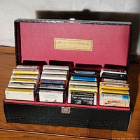 View of open black faux leather carrying case filled with 24 assorted 8-track tapes arranged in four rows.