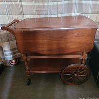 Side view of tea cart with drop leaf closed showing wood finish and wheel design.