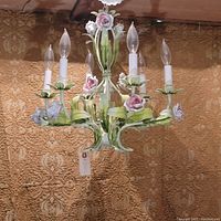 Full view of painted metal chandelier showing six candle-style lights, floral motifs and leaf scrollwork against fabric backdrop