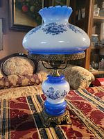 Full view of the 19-inch tall blue and white floral hurricane table lamp made of glass and brass base.