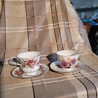Photo showing two tea cups with matching saucers placed side by side on a fabric background.