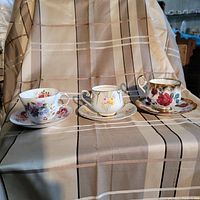 Lot of three fine bone china tea cups and saucers displayed on striped fabric.