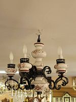 Full chandelier mounted and lit in a showroom, showing the porcelain candle holders and black iron arms.
