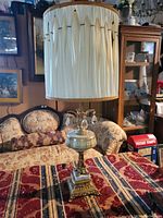 Photo showing two large vintage table lamps on a patterned tablecloth with ornate bases and cream pleated shades.