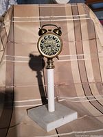 Full view of vintage brass-tone mechanical alarm clock mounted on white cylindrical stem and marble base.