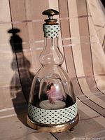 Photo of a clear glass bottle decanter with a metal top and decorative light blue polka dot bands. Visible inside the bottle is a dancing couple figurine as part of the musical box feature.