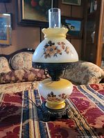 Full view of vintage side lamp showing cream-colored glass with floral painting and ornate metal base.