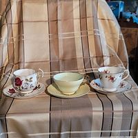 Three fine bone china tea cups and saucers with various floral patterns displayed on a plaid cloth background