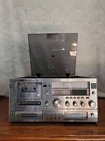 Front view of the stereo system showing cassette slot, control buttons and dials, and lift-up lid for turntable.