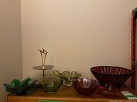 Overall view of the MCM two-tier serving stand with six colored art glass bowls in various colors and shapes on a wooden surface against a plain wall.