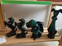 Five glazed ceramic animal figurines on wood shelf, including two rearing horses, a buffalo, a seated dog, and a tall dog with bow tie.