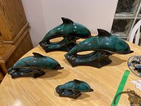 Four dolphin figurines in green and black drip glaze by Blue Mountain Pottery arranged on a wooden table.