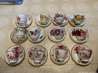 Top-down view of 10 assorted English fine china teacups and saucers arranged in rows showing floral designs and gold trims.