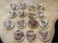 Top view of all 12 teacups and saucers arranged on floor showing different floral patterns and gold trim.