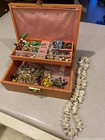 Full view of peach-colored jewelry box open showing multiple costume jewelry pieces inside and seashell necklace next to box