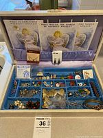 Blue velvet tray with assorted costume jewelry including earrings, pins, Christmas angel decorations, and other small items arranged in compartments.