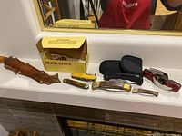 Display of all knives including Buck knife in original box, multi-tool knife, and hunting knife with sheath.