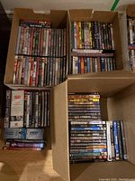 Three boxes filled with multiple DVDs featuring various movie and TV show titles, organized inside cardboard boxes