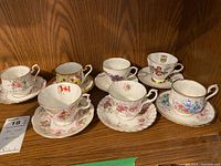 Seven fine china teacups and saucers arranged on wood shelf showing patterns, shape, and general condition.