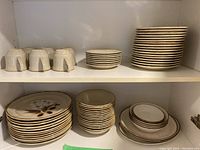 Stoneware dishes, bowls, and mugs stacked on shelves showing various sizes and types of items in set