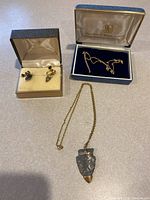 Three jewelry items: earrings in box, chain in box, and arrowhead necklace laid out